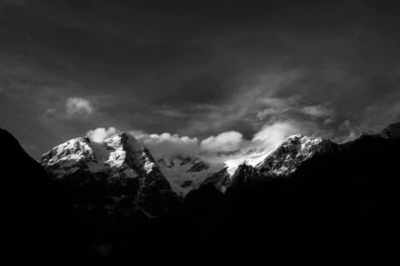 Stunning black and white photo of snow-capped mountains under a dramatic sky.