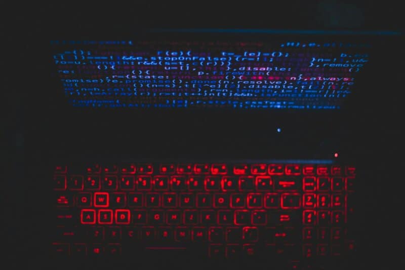 Dark-themed laptop setup with a red glowing keyboard and code on screen, ideal for tech enthusiasts.