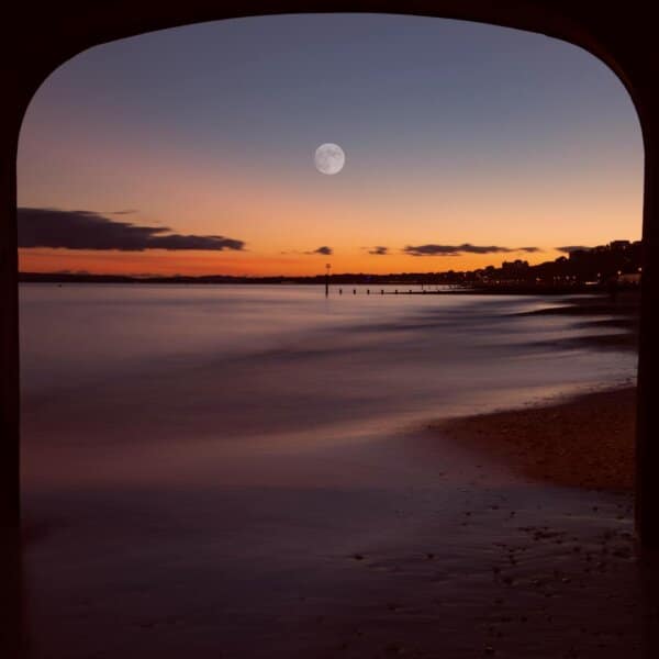 Serene sunset view at Bournemouth beach framed by a pier with a moonlit sky.