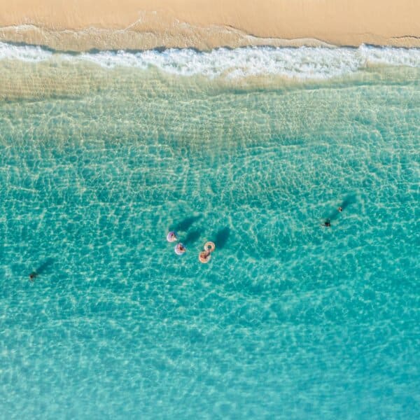 A stunning aerial shot of people enjoying swimming in turquoise waters near a sandy beach.