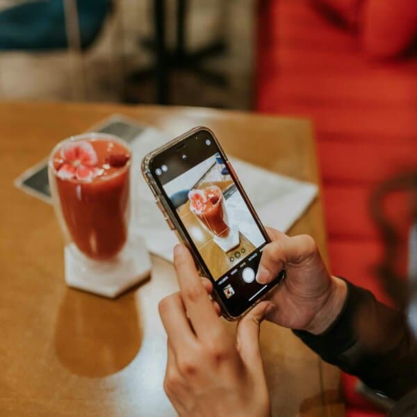Close-up of hands photographing a red smoothie with a smartphone in a cozy setting.