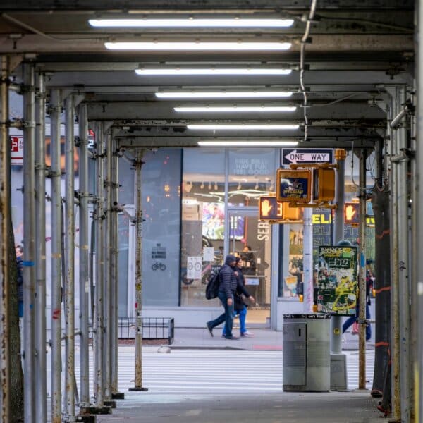 A bustling New York City street scene under scaffolding during winter with pedestrians crossing.